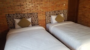Dos camas con cabeceros y almohadas con diseños, frente a una pared de ladrillo.
