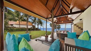 A covered outdoor seating area with a view of the ocean, a lawn, and a building in the background. - Baan Samlarn (Koh Samui)