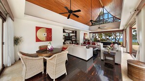 A spacious living area with a wooden ceiling, a dining table with wicker chairs, a white sofa, and a view of the ocean through large windows. - Baan Samlarn (Koh Samui)