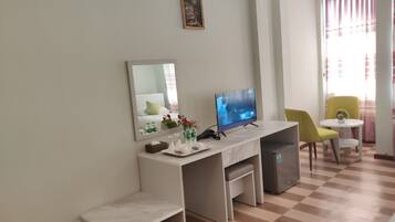 A hotel room with a desk, a television, a chair, a small table, and a trash bin.