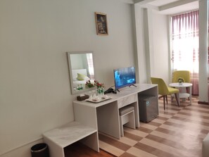 A hotel room with a desk, a television, a chair, a small table, and a trash bin.