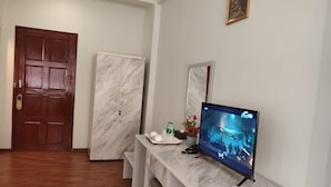 Ein Hotelzimmer mit einer Holztür, einem Marmor-Schrank, einem Fernseher auf einer Marmorplatte und einem kleinen Tisch mit Pflanze und Wasserflasche.
