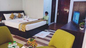 Ein Hotelzimmer mit Bett, Fernseher, Schreibtisch mit Computer und einem kleinen Tisch mit Wasserflaschen und einer Blume.