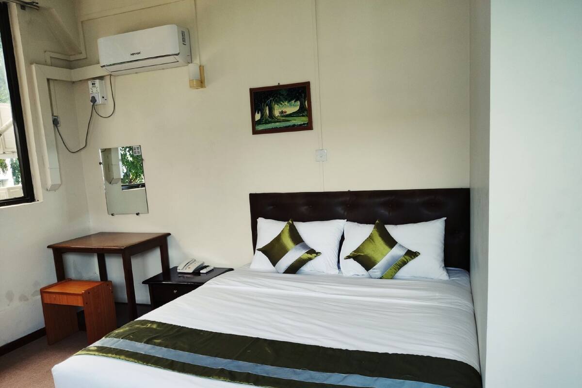 A hotel room with a bed, bedside table, and a small desk.
