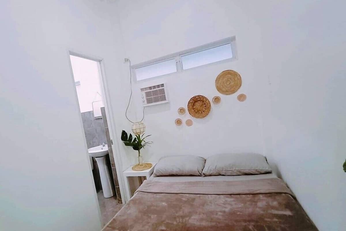 Un dormitorio pequeño y moderno con una cama individual, una mesita de noche con una planta y una ventana con persianas.