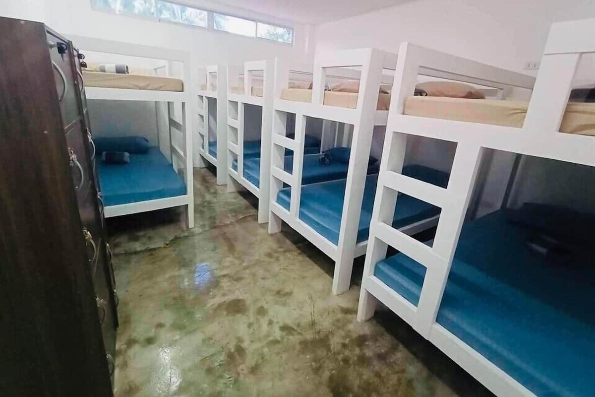 Un dormitorio con literas, suelo de hormigón y ventana que deja entrar luz natural.