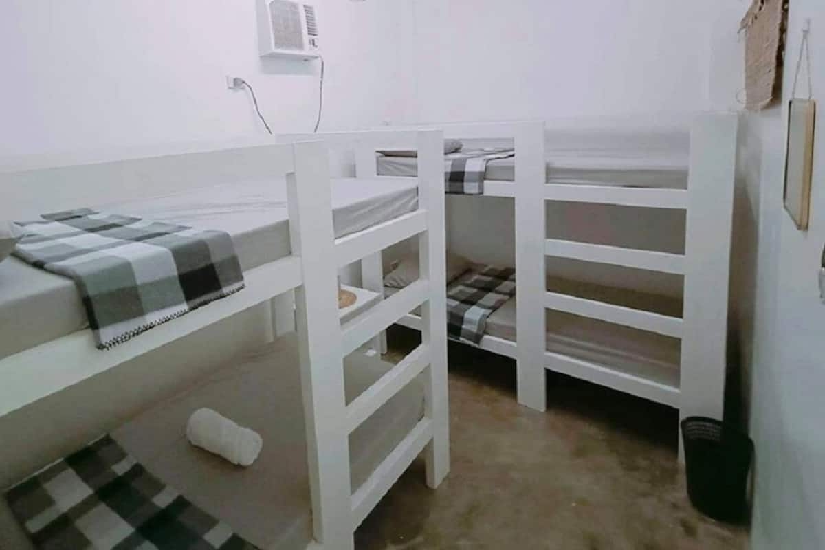 Habitación con literas, decoración en blanco, aire acondicionado de pared y un pequeño cubo de basura.