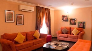 Ein Wohnzimmer mit zwei orangefarbenen Sofas, einem Glastisch und gerahmten Kunstwerken an den Wänden.