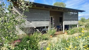 Una cabaña de madera con un porche, rodeada de un jardín con diversas plantas y flores.