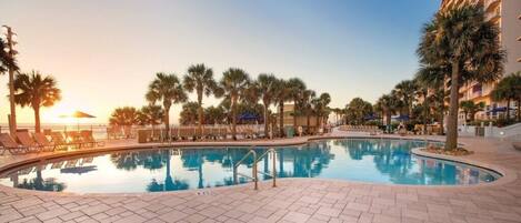 A swimming pool with lounge chairs and palm trees, surrounded by a hotel building.