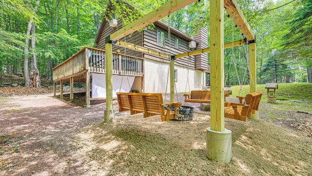 Een chalet met een houten terras, buitenmeubels en een schommel.