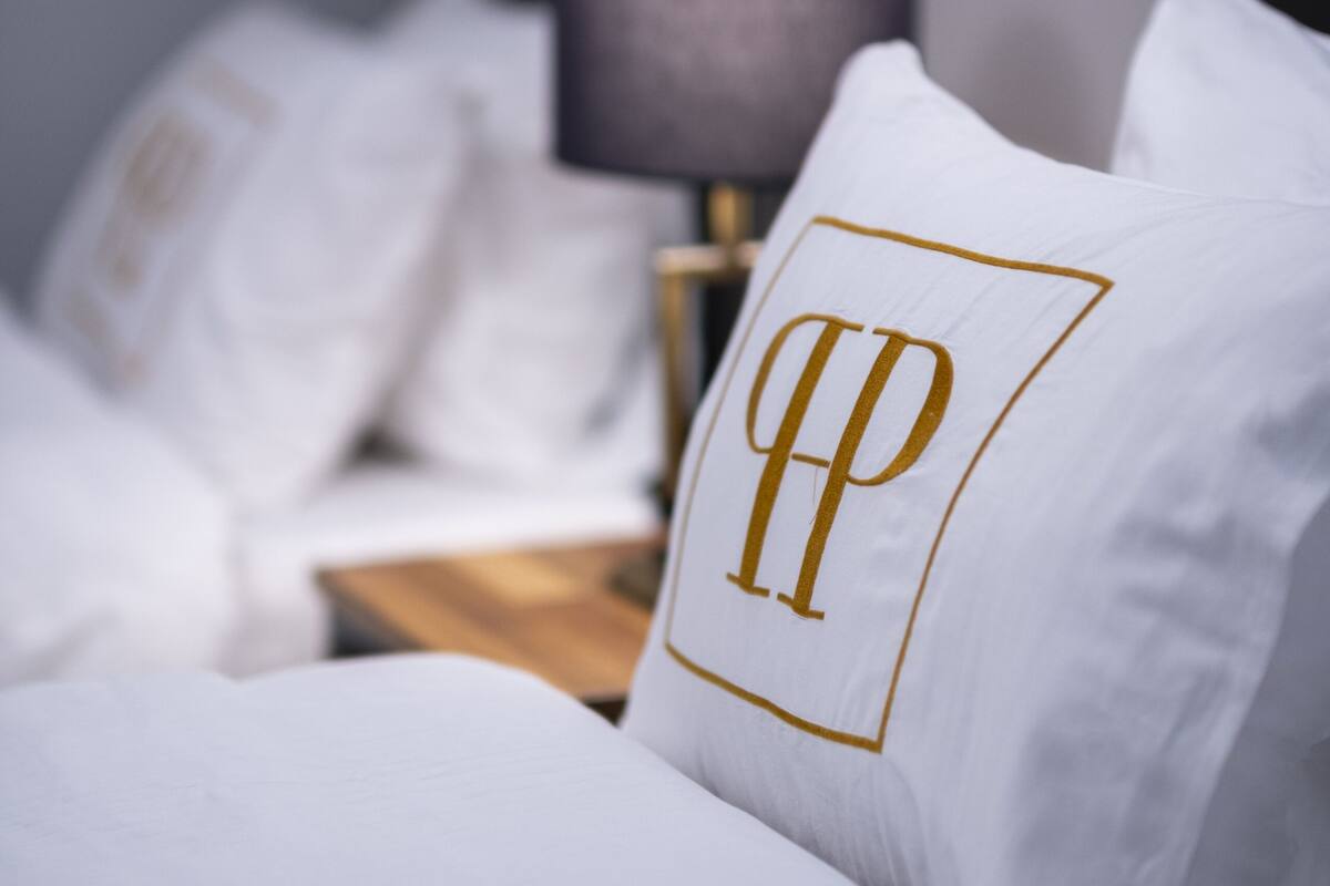 A neatly made bed with white bedding and a pillow featuring a gold monogram.