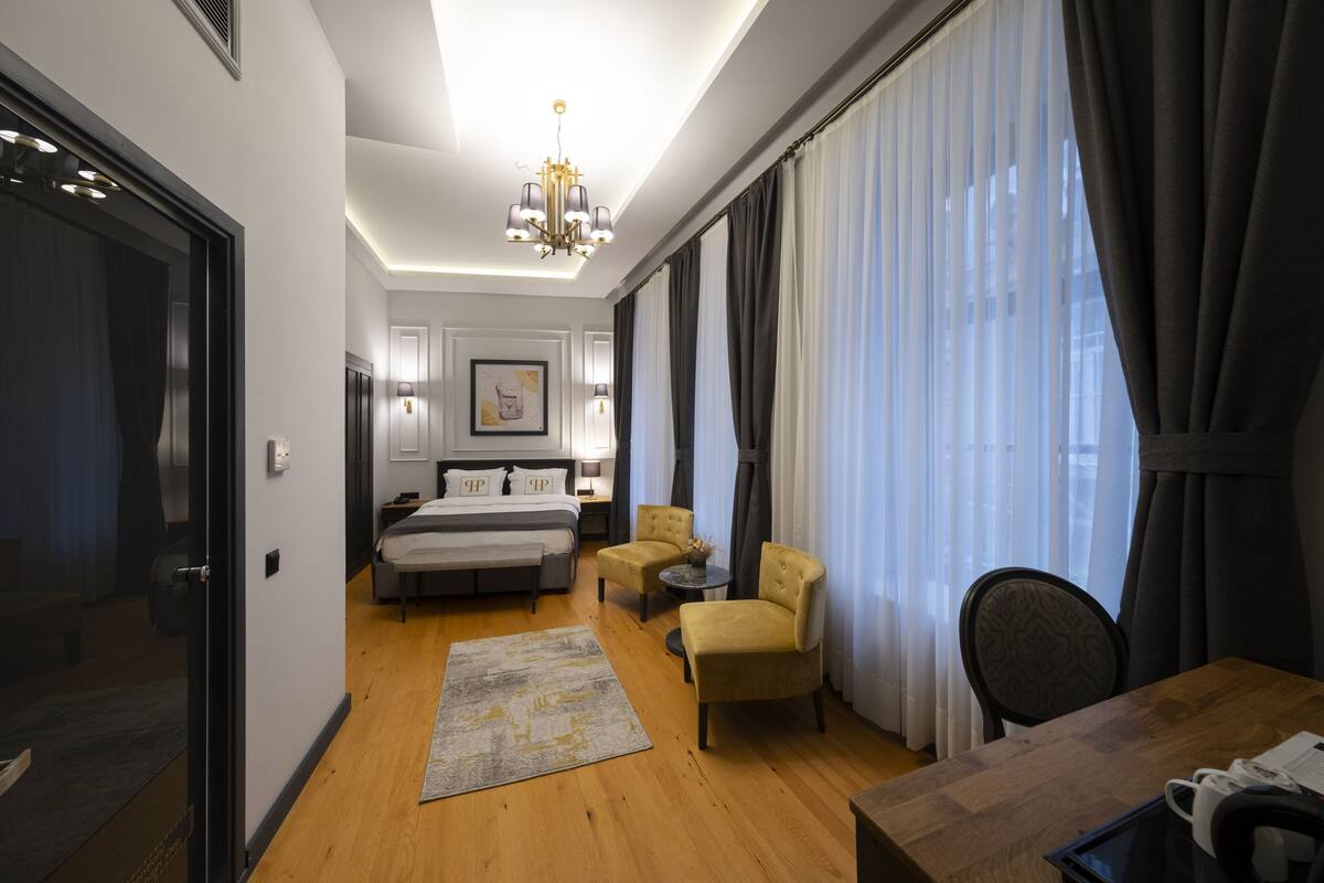 A hotel room with a bed, two armchairs, a small table, a desk, and a chandelier.