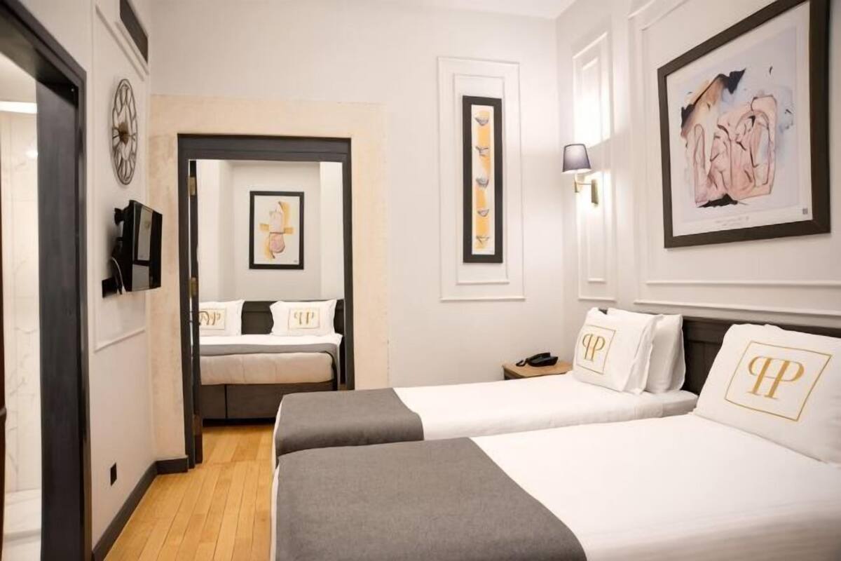 A hotel room with two beds, a desk, a chair, a clock, and artwork on the walls.