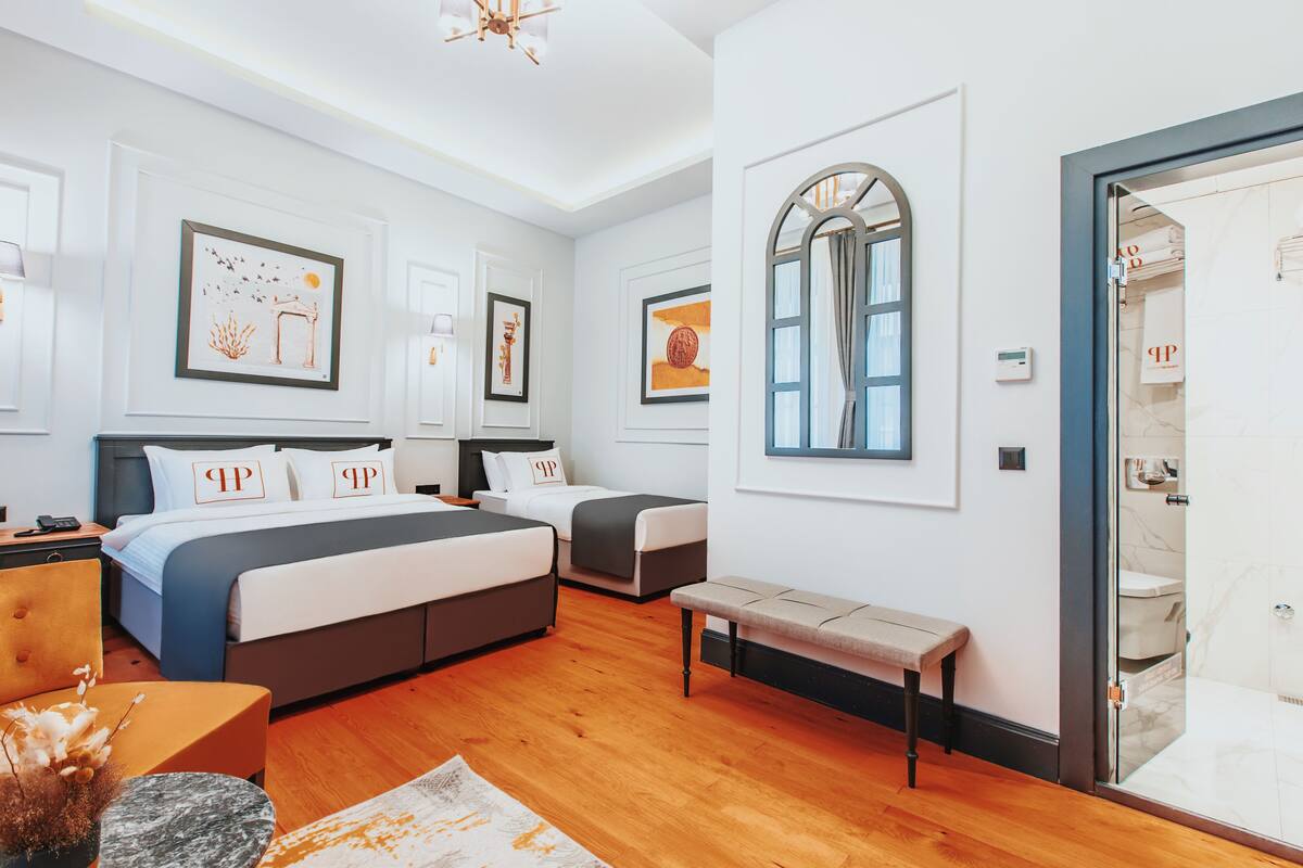 A hotel room with two beds, a bench, a small table, and artwork on the walls.