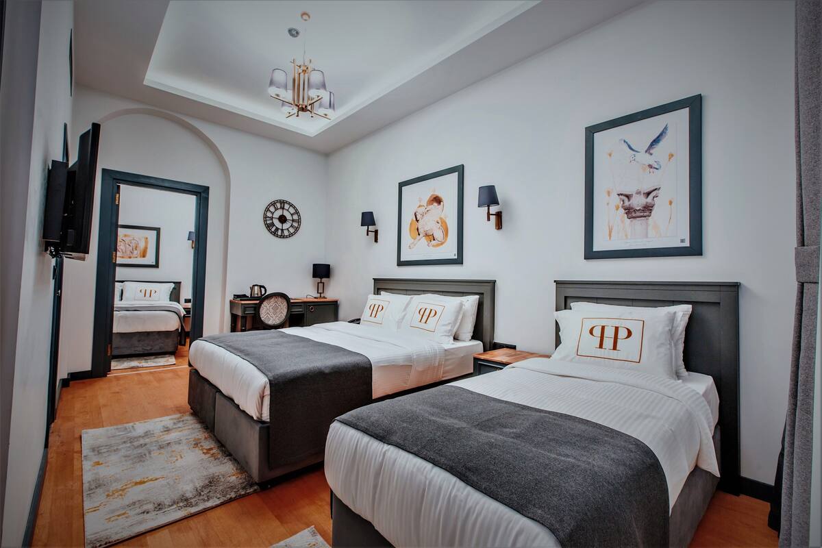 A modern hotel room with two beds, a large mirror, a chandelier, and artwork on the walls.