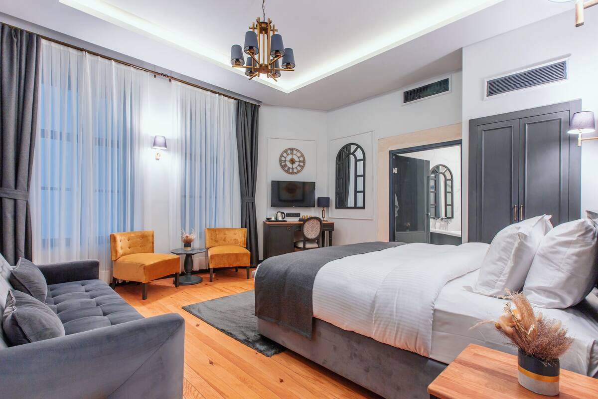 A modern hotel room with a large bed, a sofa, a desk, and a television.