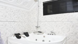 A modern bathroom with a freestanding bathtub, a showerhead, and a window with blinds. - Elim Top Suites (Jos)