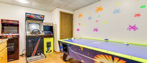 Una habitación con mesa de billar, juegos de arcade y una pared decorada con motivos espaciales.