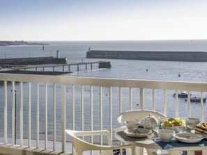 Un balcon avec une table dressée pour le petit-déjeuner, donnant sur une mer calme et une digue.