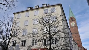 Un edificio con una torre del reloj, un cartel que dice "ARULLO'S Pizza" y árboles desnudas en primer plano.