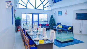 Un comedor con una larga mesa lista para una comida, un acuario de vidrio y un sofá azul.