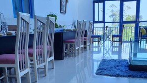 Un comedor con sillas blancas, una mesa con un tazón de canicas y vistas al exterior a través de amplias ventanas.