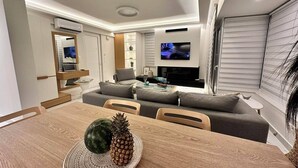 A modern living room with a dining area, a sofa, a TV, and an air conditioning unit. - POPIS SEA VIEW APARTMENTS ¨MARIRENA 2¨ (Mades Maleviziou, Heraklion, Crete)