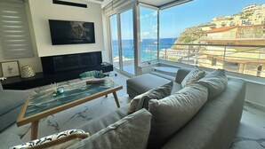 A modern living room with a large window overlooking a coastal view, a flat-screen TV, and a cozy seating area. - POPIS SEA VIEW APARTMENTS ¨MARIRENA 2¨ (Mades Maleviziou, Heraklion, Crete)