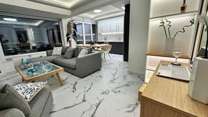 A modern living room with a grey sofa, a glass coffee table, and a wooden side table. - POPIS SEA VIEW APARTMENTS ¨MARIRENA 2¨ (Mades Maleviziou, Heraklion, Crete)