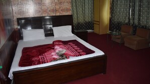 A neatly made bed with a red blanket, a wooden headboard, and a brick-patterned wall behind it. - Marina Inn Guest House (Abbottabad)