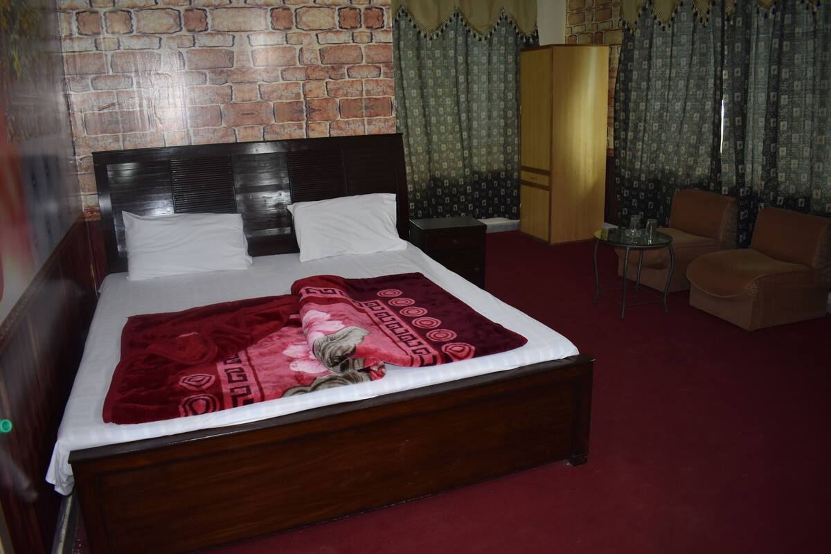 Cama bem arrumada com manta vermelha, cabeceira de madeira e parede com padrão de tijolos ao fundo.