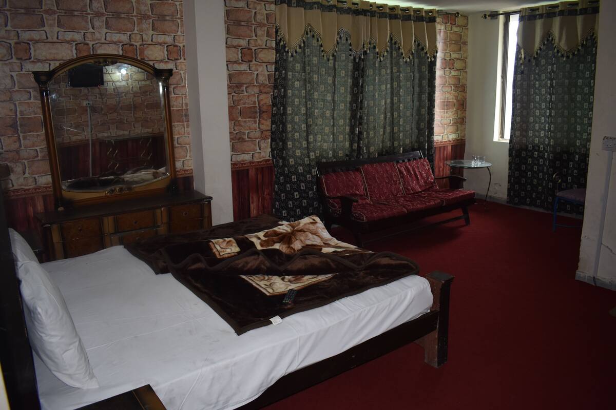 Quarto com parede de tijolos, um espelho grande, cama com colcha branca, sofá vermelho e cortinas estampadas.