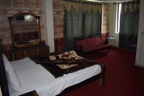 A bedroom with a brick wall, a large mirror, a bed with a white comforter, a red sofa, and patterned curtains.