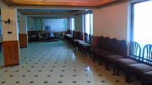 A spacious room with a tiled floor, rows of chairs, a sofa, and a large window. - Marina Inn Guest House (Abbottabad)