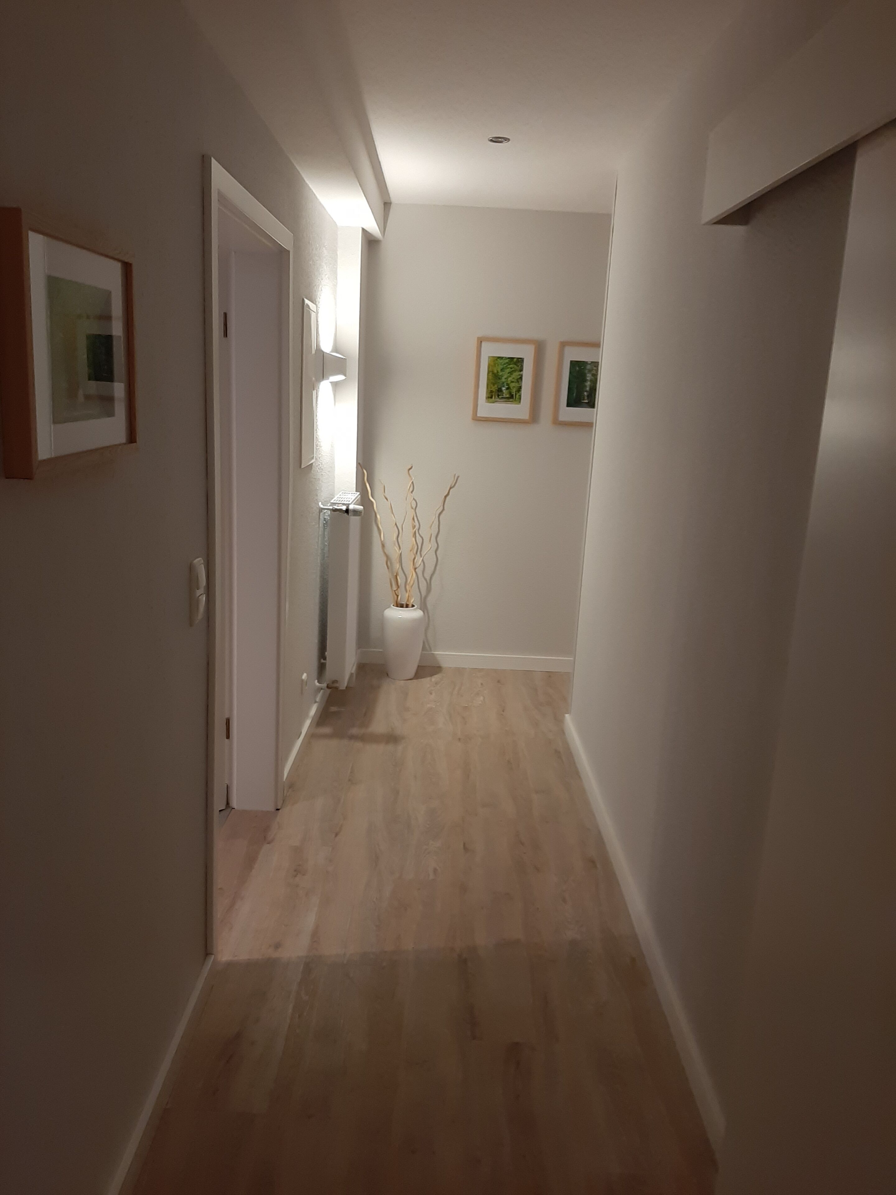 Un couloir doté d’un plancher en bois, de murs blancs et de tableaux encadrés accrochés au mur.