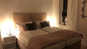 Un letto rifatto con una coperta e dei cuscini a fantasia, un comodino con una lampada e una finestra con tende.
