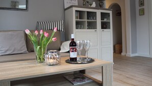 Un soggiorno con un tavolino in legno, un vaso con tulipani, una bottiglia di vino e due bicchieri. Si vede un divano con cuscini a righe e un mobile con ante in vetro sullo sfondo.