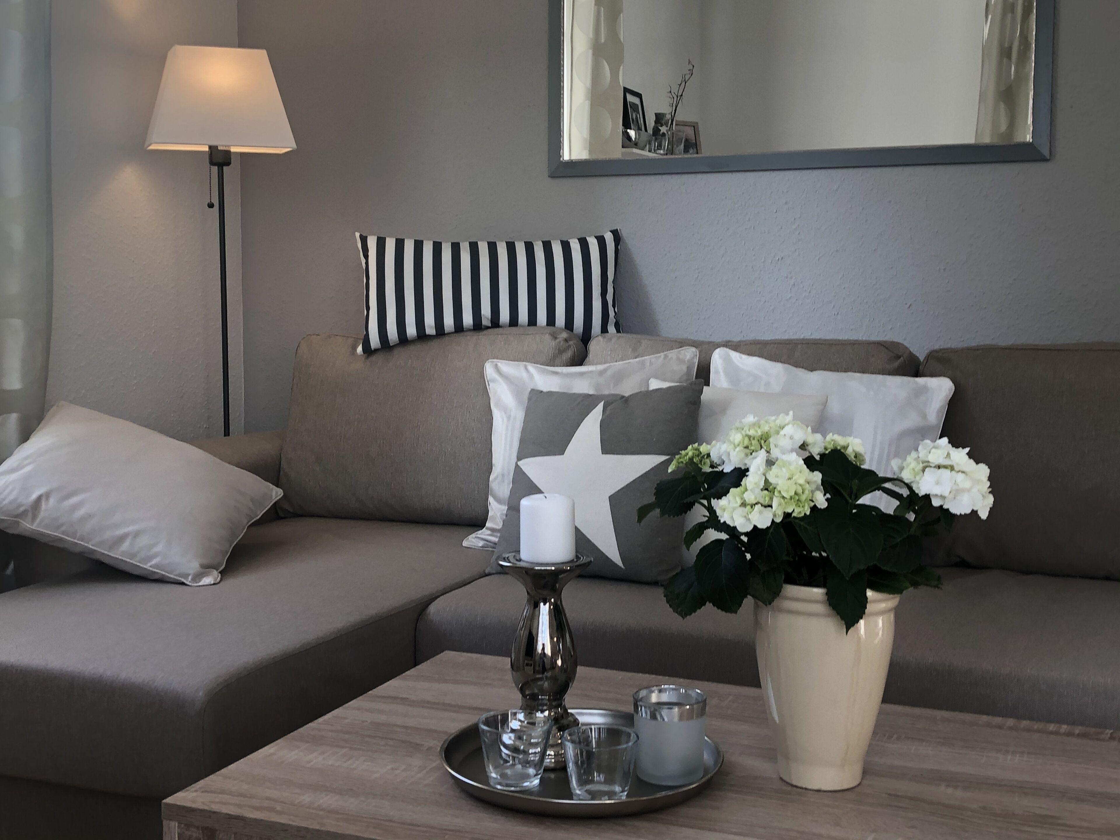 A living room with a sofa, pillows, a tray with candles, and a vase with flowers.