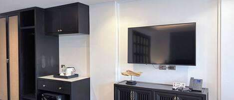 A modern hotel room with a flat-screen TV mounted on the wall, a small desk with a telephone, and a cabinet with a mirror.