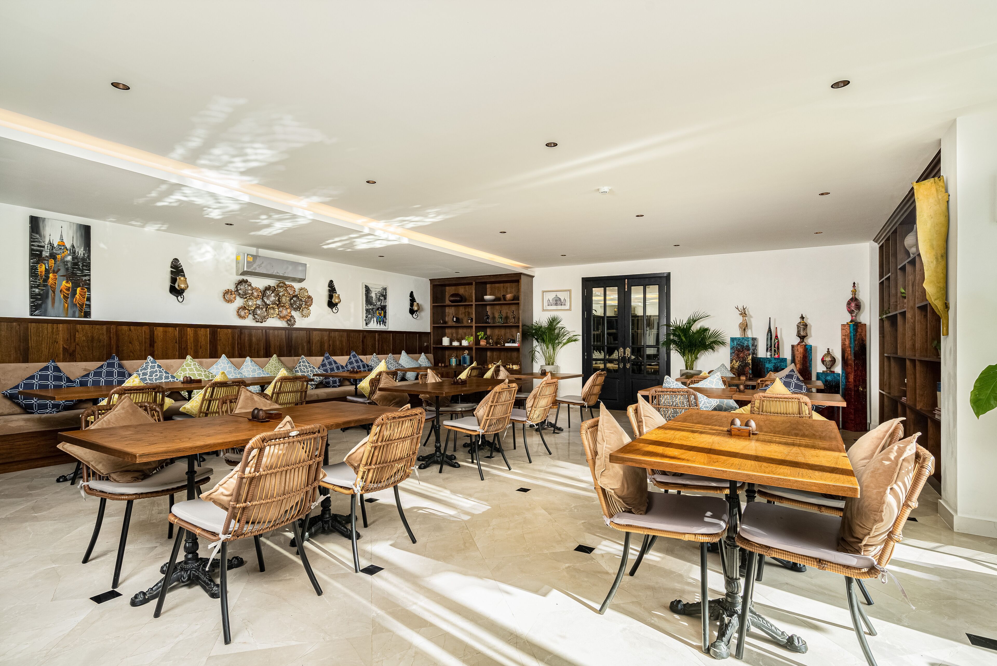 Un comedor amplio con varias mesas de madera y sillas de mimbre, rodeado de decoración en las paredes y una estantería grande.