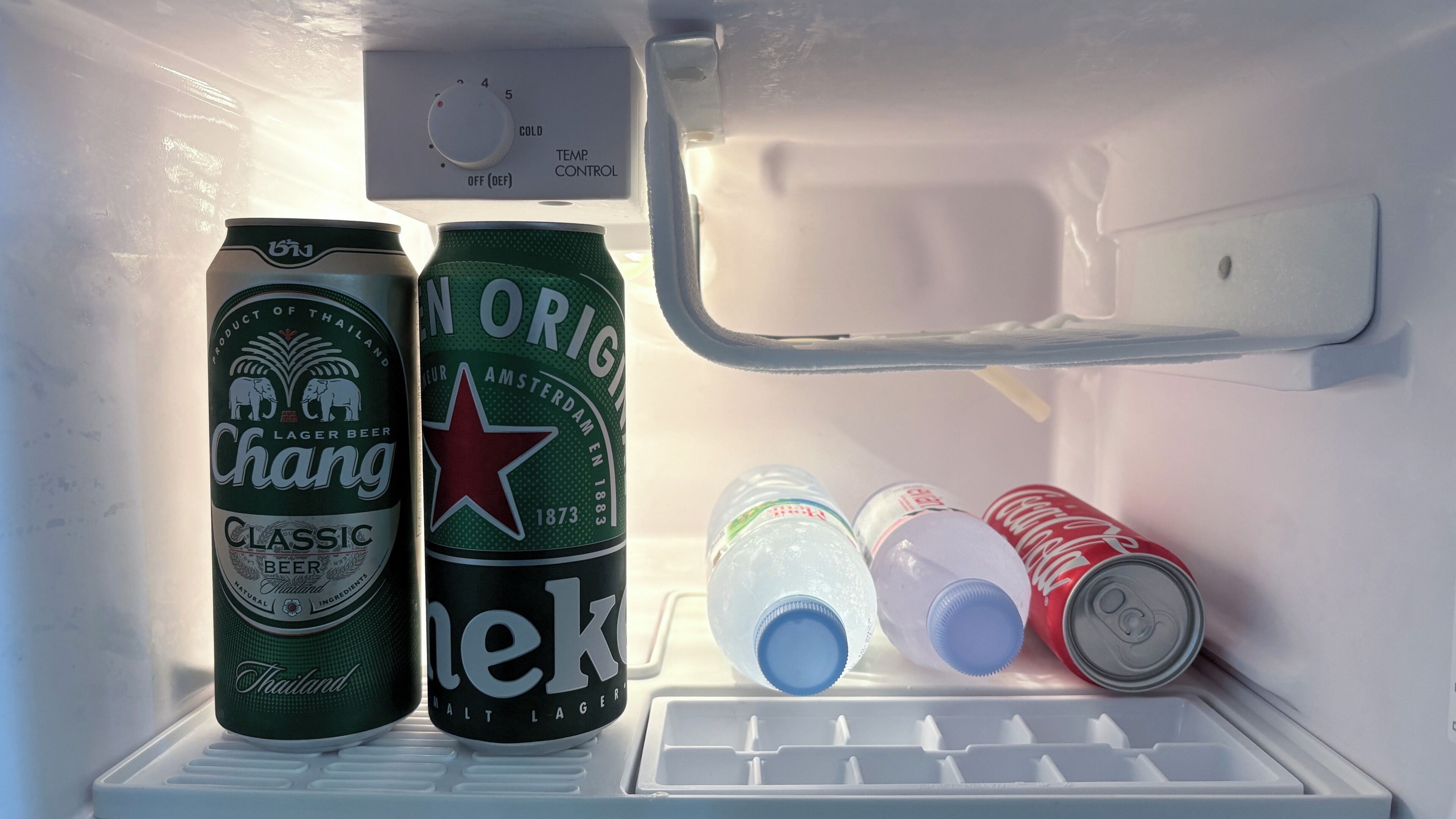 A refrigerator with two beer cans, a bottle, and a Coca-Cola can.