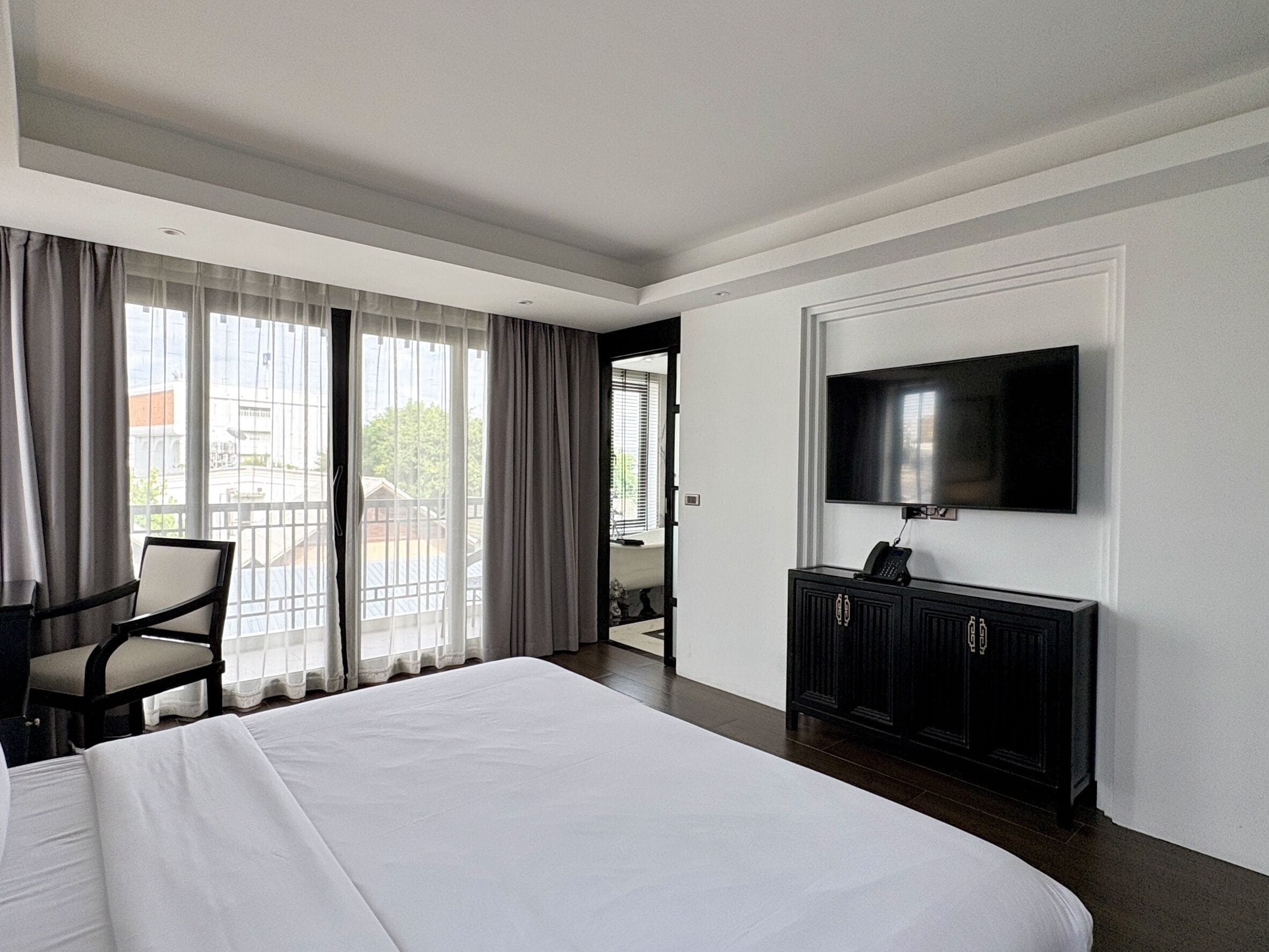 Habitación de hotel con una cama grande, televisión montada en la pared, escritorio con teléfono y vistas al exterior desde un balcón.