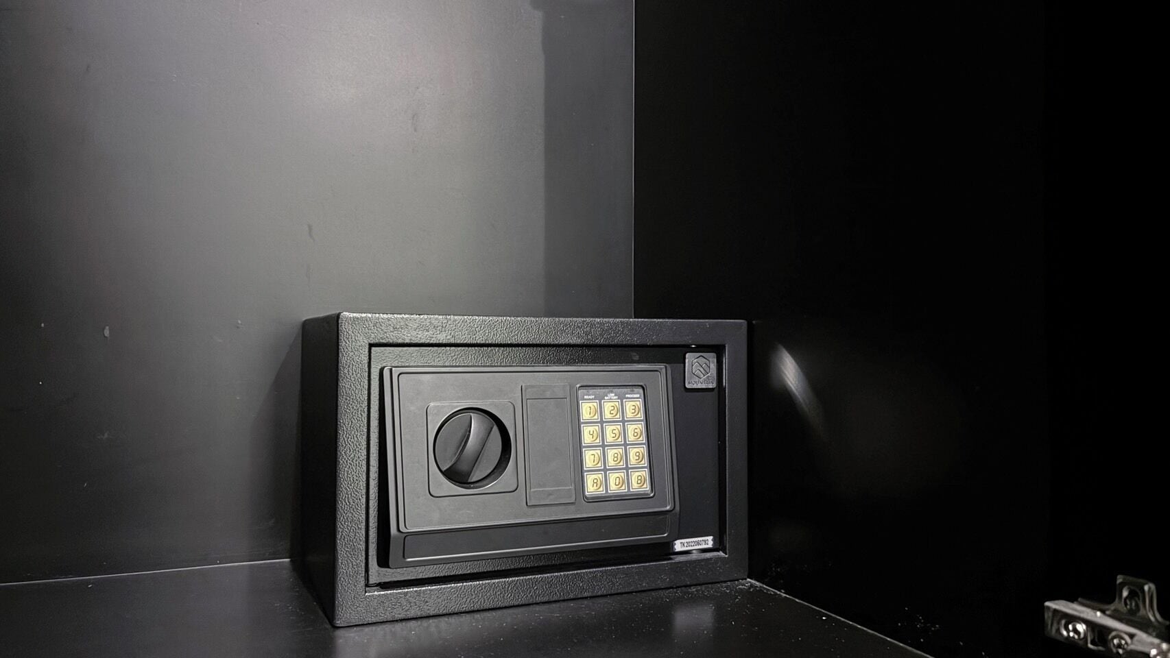 Um cofre preto com mostrador de combinação e teclado, posicionado contra uma parede escura.