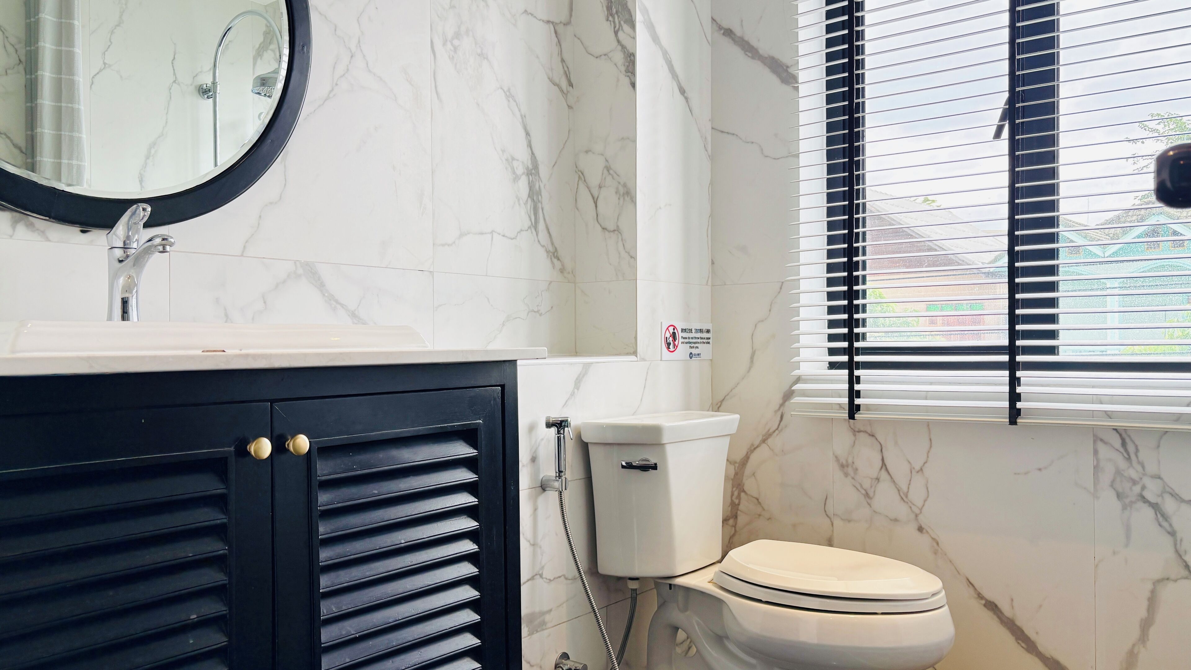 A bathroom with a marble sink, a toilet, and a window with blinds.