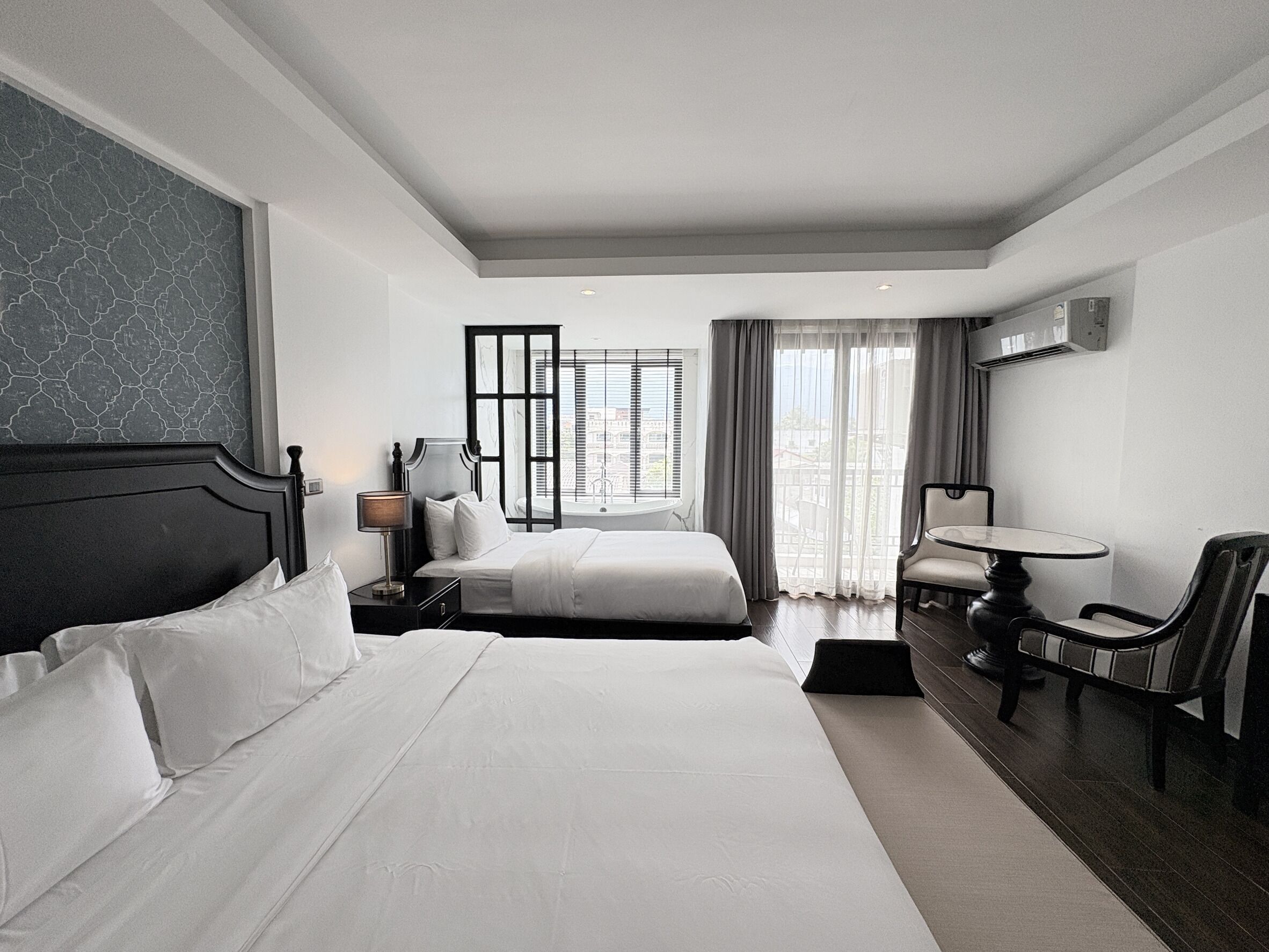 A hotel room with two beds, a desk, a chair, and a large window with curtains.