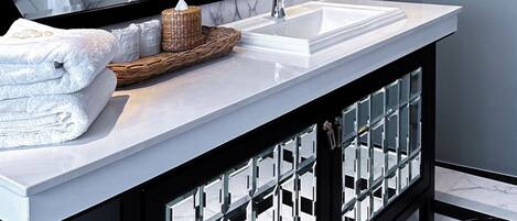 Un bagno moderno con uno specchio grande, pareti in marmo, un lavandino bianco e un mobile contenitore nero.