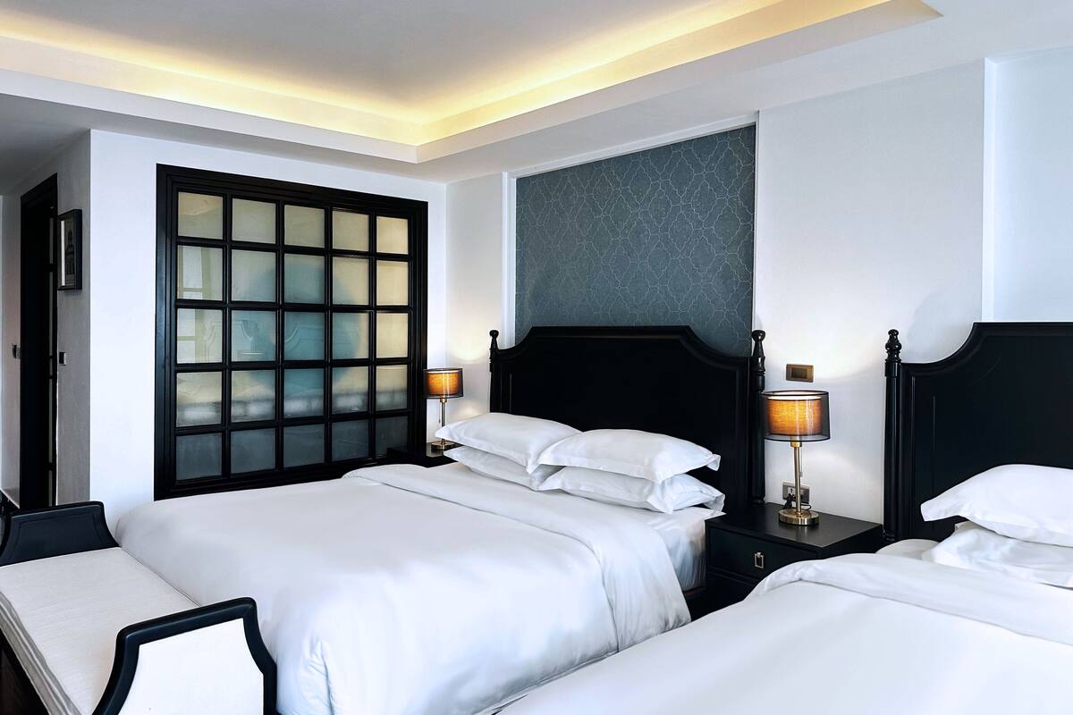 Habitación de hotel con dos camas, un ventanal grande con vidrio esmerilado y un cabecero oscuro.