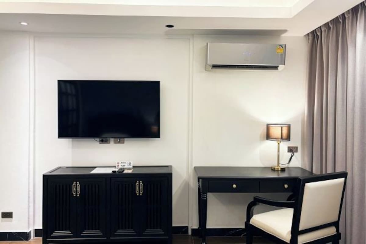 Habitación de hotel con televisión de pantalla plana en la pared, un escritorio con lámpara y una silla.