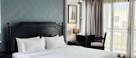 Une chambre d’hôtel avec un grand lit, un bureau, une chaise, une lampe et une fenêtre avec des rideaux.